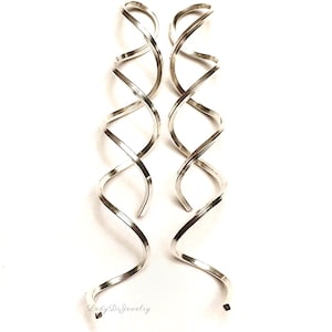 May include: A pair of silver spiral earrings. The earrings feature a long, twisted design, similar to a double helix. They are presented against a white backdrop. These earrings are a type of jewellery.