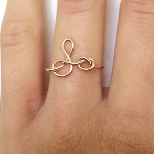 Puede incluir: Un anillo de color dorado con un diseño delicado e entrelazado. El anillo se lleva en un dedo.