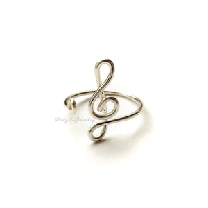 May include: Silver treble clef ring. The ring is made of wire and is shaped like a treble clef. It is a simple and elegant design.