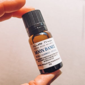 May include: A small brown glass bottle with a black cap, labeled "Carth Touif Nature Based Wellness Moon Dance Sea Salt - Cedarwood - Patchouli Add 10-12 drops to water in an electric diffuser or 12 drops onto a hanging clay or wood diffuser.  100% Phthalate Free Premium Fragrance Oil 10 ml."