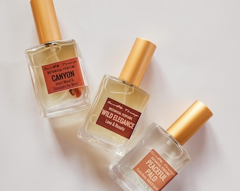 May include: Three glass bottles of botanical perfume with gold caps. The bottles are labeled "Canyon", "Wild Elegance", and "Peaceful Palo".