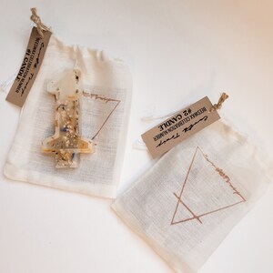 May include: Two small white fabric bags with brown paper tags. The bags contain beeswax candles. The tags have the text "#1 CANDLE BEESWAX CELEBRATION NUMBER" and "#2 CANDLE BEESWAX CELEBRATION NUMBER".