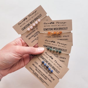 May include: Four cards with brown paper backgrounds and white text. Each card features a different gemstone wish bracelet with a description of the stone and its meaning. The bracelets are made with natural hemp string and gemstones. The text on the cards reads "Earth Tonif", "Nature Based Wellness", "Gemstone Wish Bracelet", "Make a wish, tie bracelet onto wrist or ankle, trim excess string & enjoy!" and "Tag EarthTonix in your photos".