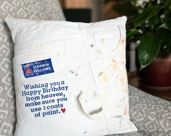 Może przedstawiać: Biała poduszka z kieszenią z dżinsu poplamioną farbą. Kieszeń ma niebieskie logo Sherwin Williams i ręcznie napisany napis "Wishing you a Happy Birthday from heaven, make sure you use 2 coats of paint."