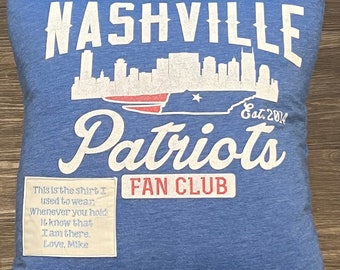 Może przedstawiać: Niebieska poduszka z białym tekstem, który brzmi "Nashville Patriots Fan Club Est. 2014". Poduszka przedstawia białą sylwetkę panoramy Nashville i czerwono-biało-niebieską flagę amerykańską. Mała biała metka przymocowana do poduszki głosi "This is the shirt I used to wear, Whenever you hold it know that I am there Love, Mike".
