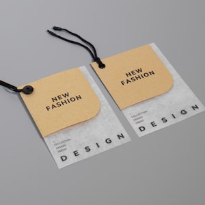 May include: Two clothing tags with the words "NEW FASHION" printed on a tan background. The tags have a white, semi-transparent base with the word "DESIGN" printed in black. Black string is attached to the tags.