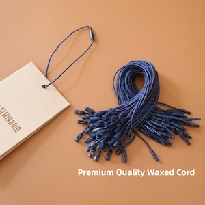May include: A beige tag with the word "SEMINARIO" printed on it, attached to a bundle of navy blue waxed cords with plastic fasteners. The text "Premium Quality Waxed Cord" is at the bottom of the image.