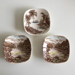 May include: Three square ceramic dishes with rounded corners, each featuring a detailed brown and white transferware landscape scene. The top dish depicts a water mill with the text Water Mill, while the two bottom dishes show village scenes.