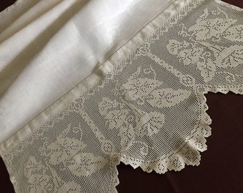 May include: Ivory-colored lace fabric with a floral pattern and scalloped edge. The lace is detailed with openwork and is attached to a smooth, folded fabric. The overall design suggests a vintage or antique textile.