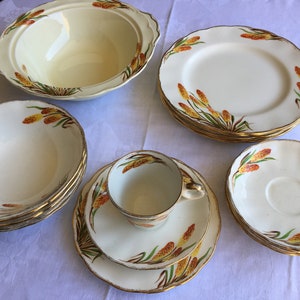 May include: A vintage cream-coloured china set with a wheat-like design in yellow, orange, and green. The set includes plates, bowls, a serving bowl, a teacup, and saucers, all with gold trim.