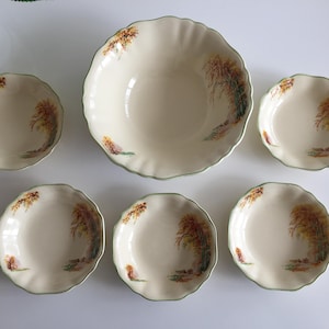 以下が含まれることがあります： クリーム色のセラミック製サービングボウルと、それに合う5つの小皿。各ピースはスカラップエッジと、秋の色で描かれた風景画が特徴です。セットは緑色のトリムが付いています。