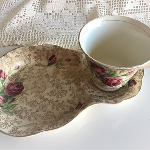 May include: A vintage teacup and saucer set with a floral pattern featuring pink roses and gold accents. The saucer is shaped like a leaf and has a scalloped edge.