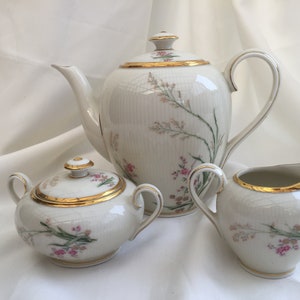May include: A white porcelain tea set with a floral design. The set includes a teapot, creamer, and sugar bowl. Each piece has a gold trim and a delicate floral pattern.