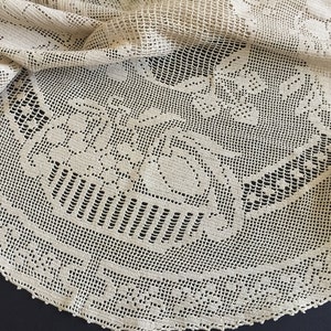 Könnte beinhalten: Eine weiße Häkeltischdecke mit einem zarten Blumendesign. Die Tischdecke ist rund und hat einen gewellten Rand.