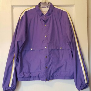 May include: A purple jacket with white and yellow stripes down the sleeves. The jacket has a button-up front and a small pocket on the front.