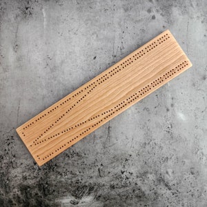 May include: A wooden cribbage board with a natural wood finish. The board has a series of holes for pegs and a scoring track.