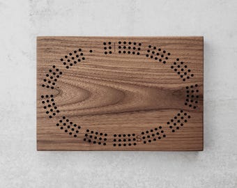 May include: A wooden board with a circular pattern of small holes cut into the surface. The board is made of walnut wood and has a natural brown color.