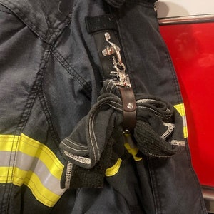 May include: A black firefighter jacket with a yellow reflective stripe and a black leather strap with a silver hook attached to it.