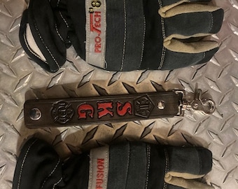 May include: Two pairs of black and tan firefighter gloves with the text "Pro-Tech 8 Fusion" on the wrist straps. A brown leather keychain with the text "S.K.G." and a firefighter emblem is in the center of the image.