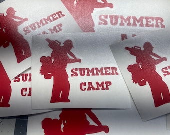 Può includere: Un mucchio di adesivi bianchi con una silhouette rossa di una persona che porta un'altra persona sulla schiena. Gli adesivi dicono "Summer Camp" in lettere rosse.