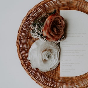 May include: A wicker basket with a white and brown floral arrangement and a white card with the text "To Dine" on it.