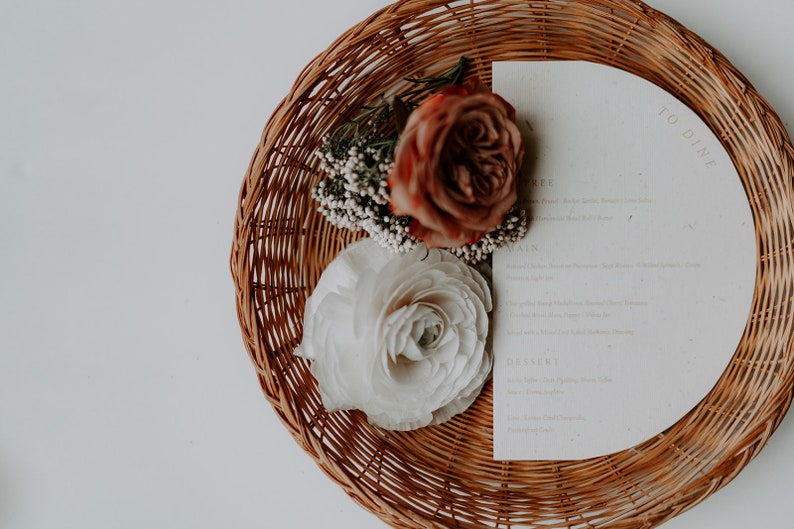 May include: A wicker basket with a white and brown floral arrangement and a white card with the text "To Dine" on it.