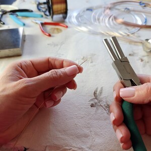 A person's hands are holding a pair of pliers and a piece of wire, presumably working on a craft or DIY project.