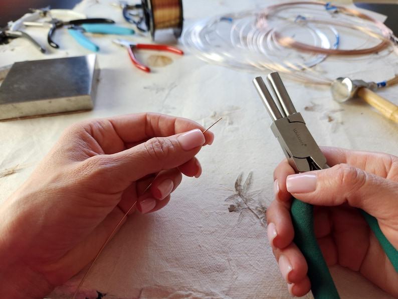 A person's hands are holding a pair of pliers and a piece of wire, presumably working on a craft or DIY project.