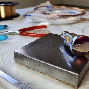 a workspace with various tools and materials, including a hammer, pliers, and copper wire, suggesting a crafting or metalworking project.