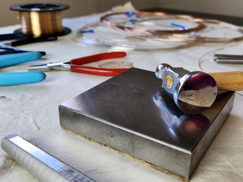 a workspace with various tools and materials, including a hammer, pliers, and copper wire, suggesting a crafting or metalworking project.