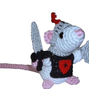 May include: A crocheted white mouse dressed as a knight, complete with a gray helmet, shield, and sword. The mouse wears a black tunic with a red heart-shaped emblem. The mouse has pink ears, nose, and feet, and a long pink tail.
