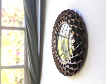 Puede incluir: Un espejo redondo de madera marrón con un diseño geométrico. El espejo refleja una ventana con vista a árboles y cielo.