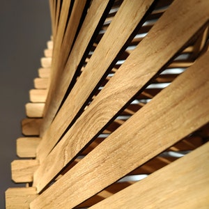 May include: A close-up of a wooden structure made of thin, light brown slats. The slats are arranged in a curved pattern, creating a spiral effect.