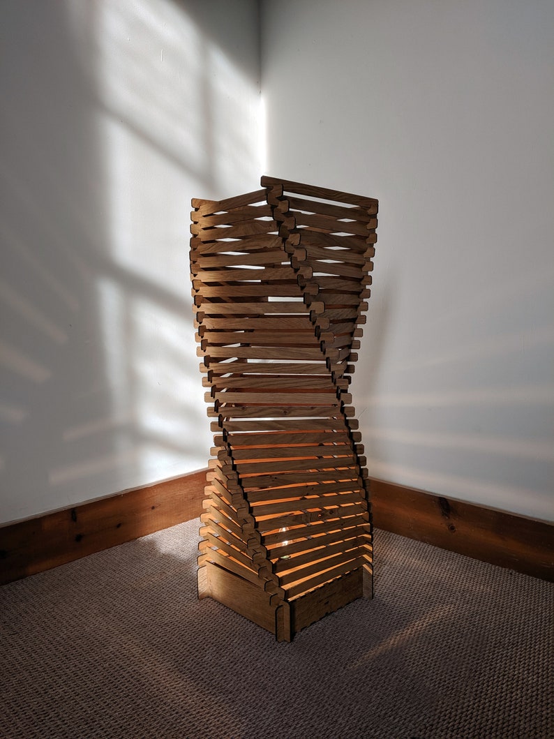 May include: A wooden floor lamp with a unique twisted design. The lamp is made of multiple slats of wood that are stacked and interlocked to create a spiral shape. The lamp is lit by a light bulb inside the base.