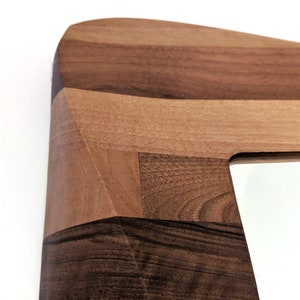 May include: Close-up of a wooden mirror frame with a geometric design. The frame is made of different shades of brown wood, creating a unique and modern look.
