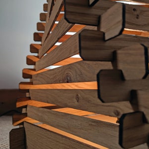 May include: A wooden lampshade with a geometric design. The lampshade is made of thin strips of wood that are stacked on top of each other. The lampshade is lit from the inside, creating a warm glow.