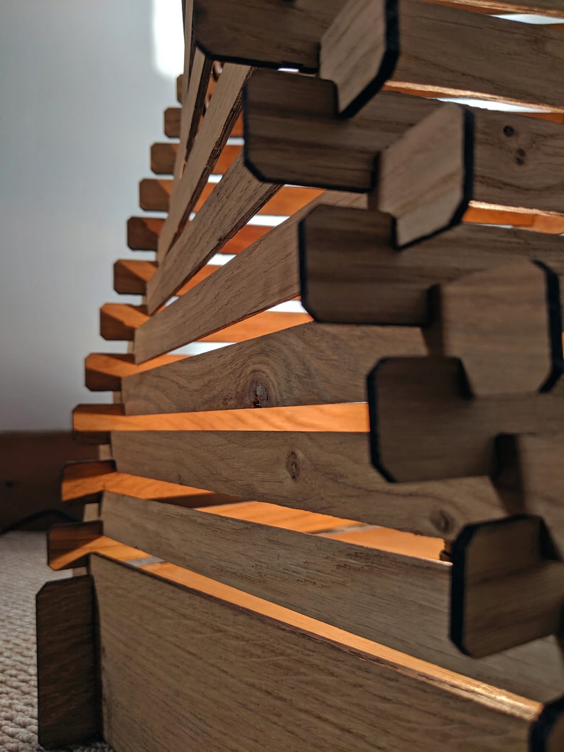 May include: A wooden lampshade with a geometric design. The lampshade is made of thin strips of wood that are stacked on top of each other. The lampshade is lit from the inside, creating a warm glow.