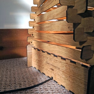 May include: A wooden lamp with a geometric design. The lamp is made of multiple pieces of wood that are stacked on top of each other. The lamp has a black cord and a label that reads "Surrey Woodsmiths".