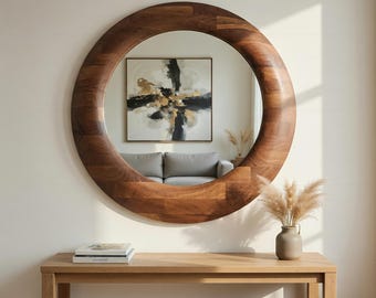 May include: A large, round wooden mirror with a thick, dark brown frame hangs on a white wall. The mirror reflects a living room scene with a gray sofa and abstract artwork. A wooden console table sits below the mirror.
