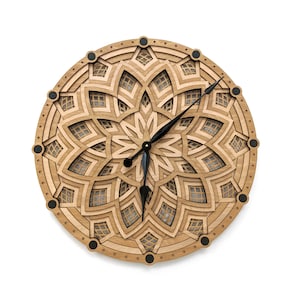 Op de afbeelding: Een ronde houten wandklok met een gelaagd, geometrisch ontwerp. De klok heeft een natuurlijke houten afwerking met zwarte wijzers en zwarte accenten. De diameter van de klok is ongeveer 30 cm.