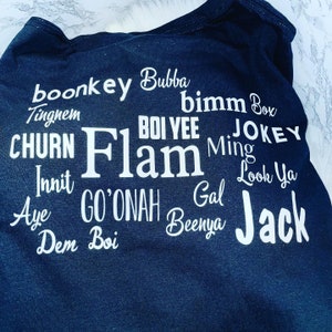 May include: Black t-shirt with white text printed on it. The text includes the words "boonkey", "Bubba", "bimm Box", "BOI VEE", "CHURN", "Flam", "Ming", "JOKEY", "Innit", "GO'ONAH", "Gal", "Look Ya", "Aye", "Dem", "Boi", "Benya", and "Jack".