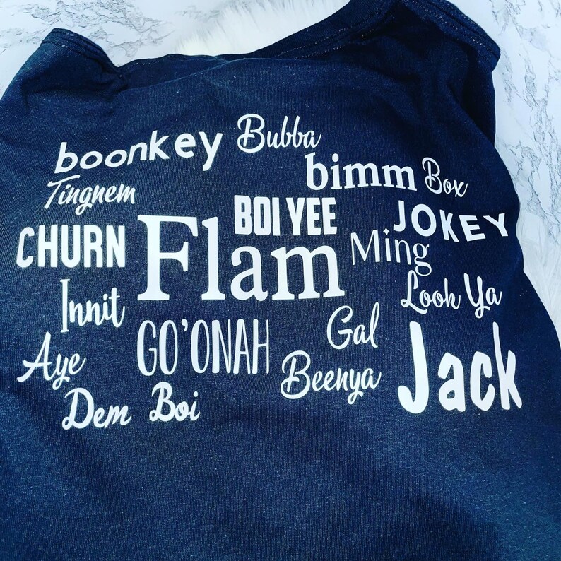 May include: Black t-shirt with white text printed on it. The text includes the words "boonkey", "Bubba", "bimm Box", "BOI VEE", "CHURN", "Flam", "Ming", "JOKEY", "Innit", "GO'ONAH", "Gal", "Look Ya", "Aye", "Dem", "Boi", "Benya", and "Jack".