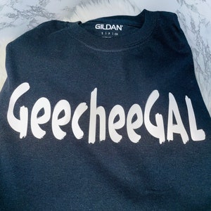 May include: Black t-shirt with white text that says "GeecheeGAL". The Gildan brand name is visible on the neck tag.