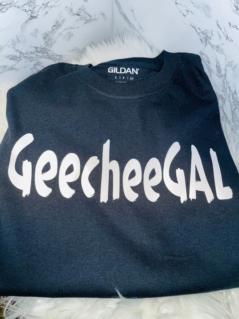May include: Black t-shirt with white text that says "GeecheeGAL". The Gildan brand name is visible on the neck tag.