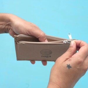 May include: A beige leather wallet with a zipper closure and the word "naga" printed on the front.
