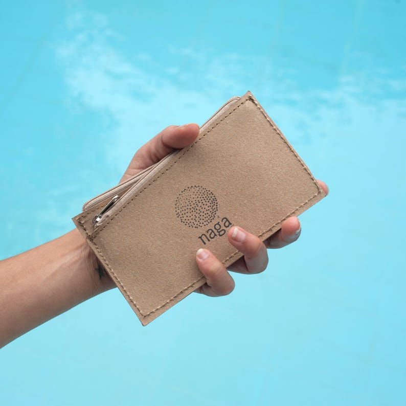 May include: A brown, zippered wallet made of recycled paper with the word "Naga" printed on the front.
