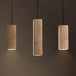 Puede incluir: Tres lámparas colgantes de madera cuelgan del techo en una sala de estar moderna. Las lámparas son de forma rectangular y tienen un acabado marrón claro. Las lámparas iluminan una mesa de café de madera.