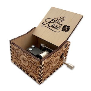 May include: Wooden music box with a floral design and the words "La Vie en Rose" engraved on the lid. The box is open and the music mechanism is visible.