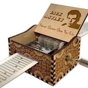 Könnte beinhalten: Holzspezielle Musikbox mit einer Handkurbel. Der Deckel ist geöffnet und zeigt ein lasergraviertes Bild von Rick Astley mit dem Text "Rick Astley Never Gonna Give You Up".