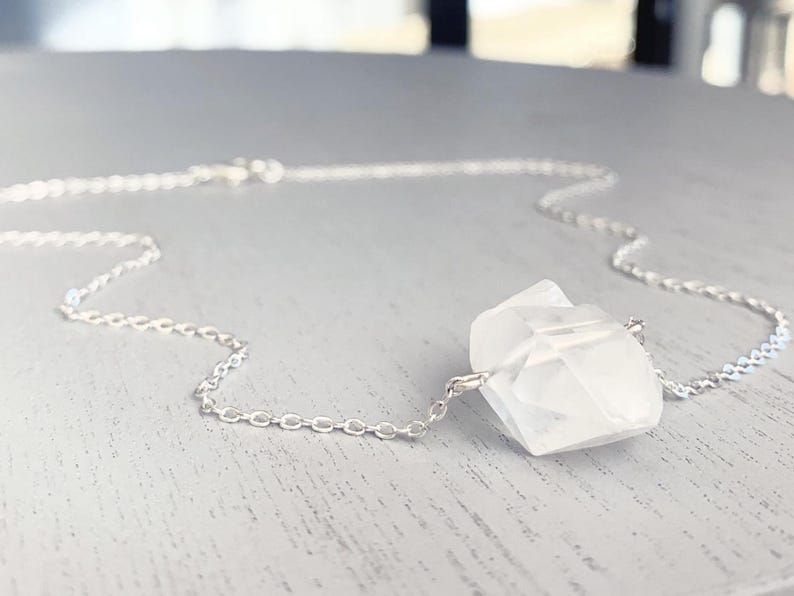 May include: A silver chain necklace with a large, clear quartz crystal pendant.